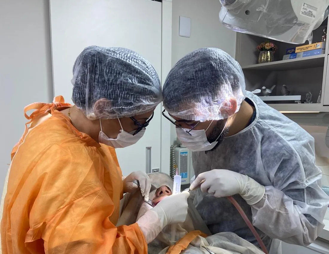 Dra. Ludmila Figueiredo e auxiliar paramentados durante procedimento cirúrgico no consultório